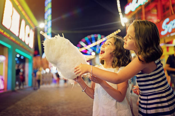 deux petites filles mangent des bonbons de coton à la foire amusante et se moquer - amusement arcade photos et images de collection