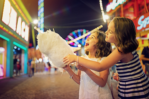 Two little girls are eating cotton candy at the fun fair and making fun