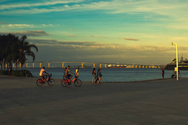 fußgänger zu fuß und mit dem fahrrad auf dem maua-platz (praça mauá auf portugiesisch), rio. im hintergrund die guanabara-bucht und die rio niterói brücke. - brazil bicycle rio de janeiro outdoors stock-fotos und bilder