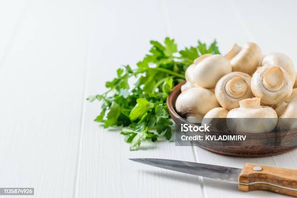 A Knife Next To A Bowl Of Mushrooms And A Bunch Of Parsley On A White Table Vegetarian Cuisine Stock Photo - Download Image Now