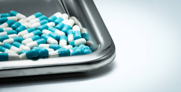 Blue-white capsule pills on stainless steel drug tray. Pharmaceutical industry. Pharmacy background. Antibiotic drug resistance. Global healthcare. Medicine for treatment infection in hospital. píldoras de cápsula azul-blanca en la bandeja de la droga del acero inoxidable. industria farmacéutica. fondo de farmacia. farmacorresistencia antibiótica. atención sanitaria global. medicamento para la infección del tratamiento en el hospital.