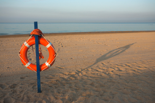 Orange emergency life saving flotation ring on the coastline with bright sunrise in background