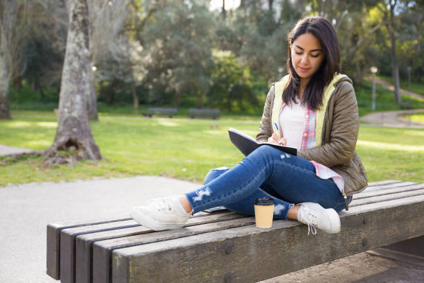 istock Pensive Asian girl making notes in diary while sitting in park 1135880980