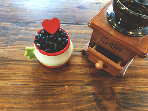 Vintage Manual Coffee grinder and Dark roast coffee beans with Red heart love in cup on the vintage wooden table. Love coffee concept. Vintage dark light style. Copy space