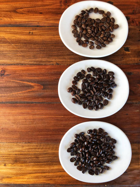 Different of coffee beans roasts between Dark roast and Medium roast. coffee beans in the white dish on the brown wooden table.