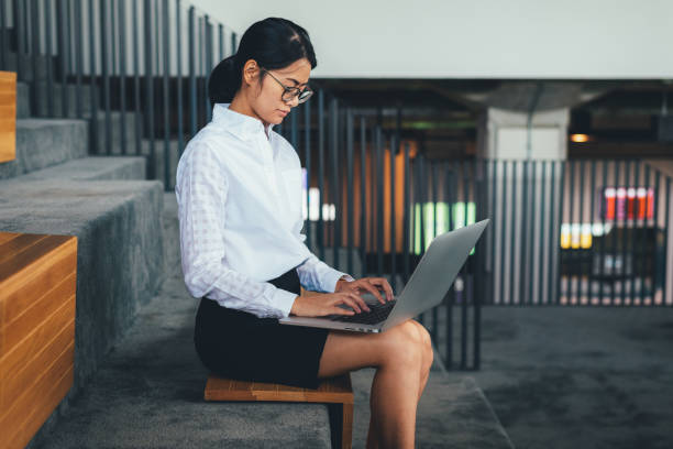 istock Asian businesswoman wear eyeglasses pay attention while using laptop working and thinking about business financial sitting on staircase at the office- woman office worker and businesswoman concept 1135898433