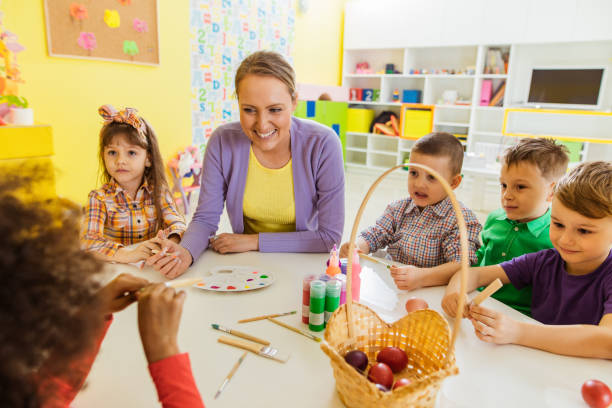 istock Happy teacher talking to preschoolers while coloring Easter eggs together. 1135906221