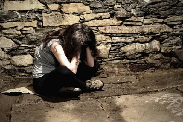 Young breakdown woman sitting on the peace of cartoon in the dark cellar, victim of violence, kidnapping or captive, view through the ajar door Young breakdown woman sitting on the peace of cartoon in the dark cellar, victim of violence, kidnapping or captive, view through the ajar door. Prisoner sexual assault stock pictures, royalty-free photos & images