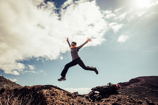 Young middle age woman jump to the stones for happiness and success concept during a travel touristic trekking - freedom and carzy modern people concept in outdoor leisure activity