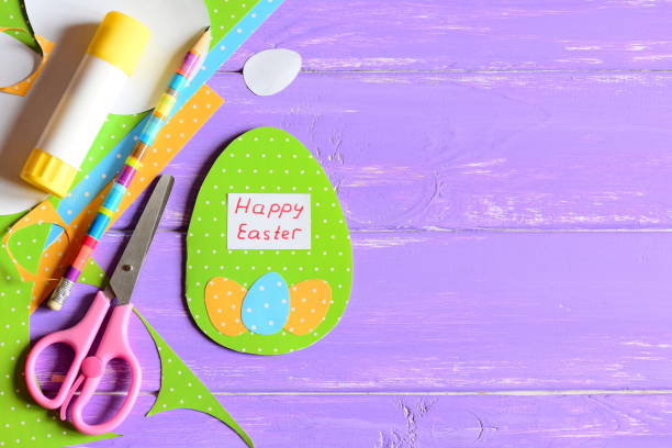 istock Happy Easter greeting card, craft tools and materials on purple wooden background with copy space for text. Cute greeting card made in form of egg with wishes Happy Easter. Bright Easter background 1135912633
