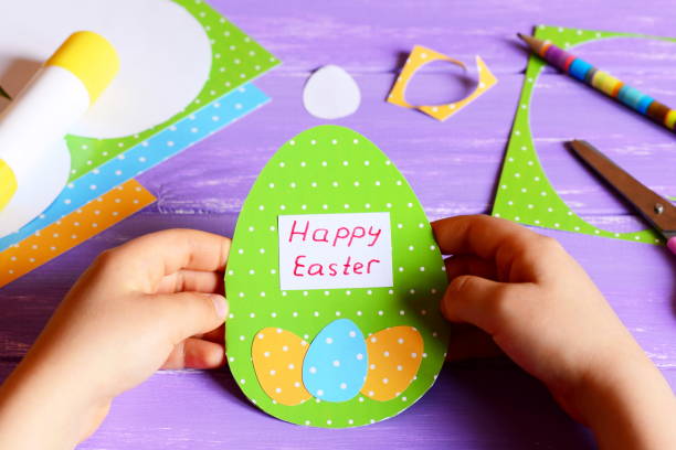 маленький ребенок держит в руках пасхальную открытку. ребенок сделал счастливую пасхальную поздравительную открытку в форме яйца. воображ - card making стоковые фото и изображения