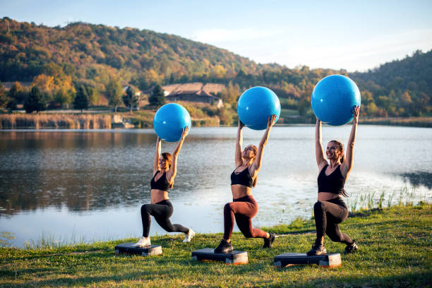 les femmes exercent à côté du lac avec le ballon. - yoga ball photos et images de collection