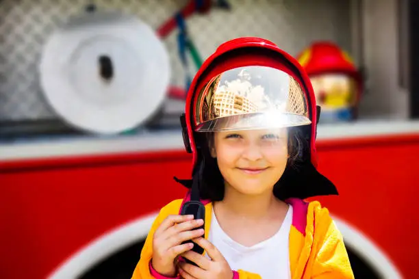 Cute young girl trying on real fireman's helmet standing in front of firetruck.