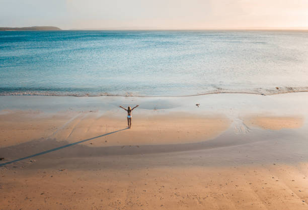 mulher que está na praia remota na luz do fim da tarde - women joy arms outstretched isolated - fotografias e filmes do acervo