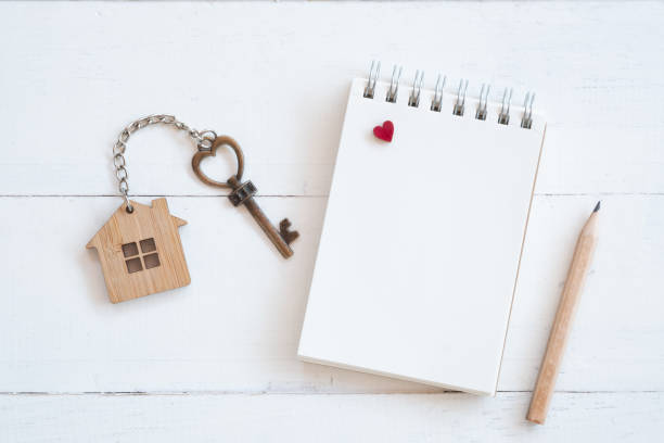 House key with home keyring, blank notebook and pencil on white wood table background, copy space stock photo