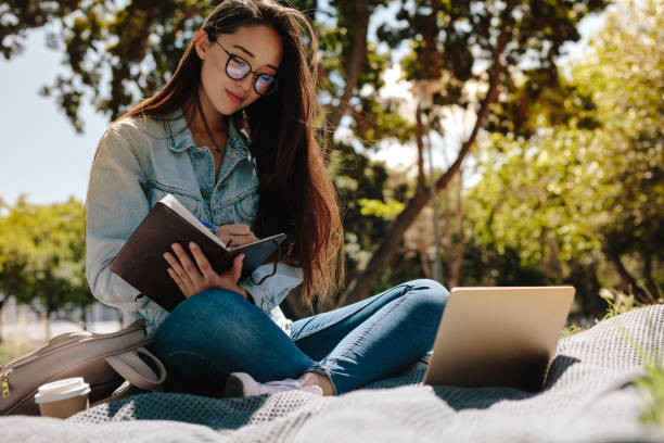 young woman studying sitting outdoors - campus life imagens e fotografias de stock