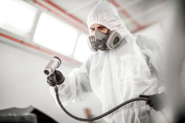 Car painting technician using a pneumatic air dryer to dry a paint on a car section in a painting chamber.