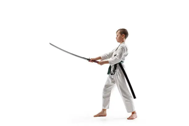 Teen boy fighting at Aikido training in martial arts school. Healthy lifestyle and sports concept. Fightrer in white kimono on white background. Karate man with concentrated face in uniform.