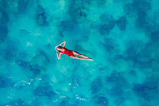 Aerial view of young woman in red swimsuit relaxing in the sea over coral reef. Happy island lifestyle. Vacation at Paradise. Ocean relax, travel to Thailand
