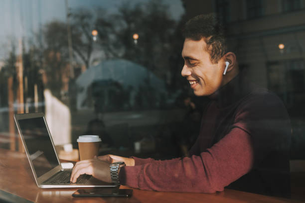 istock Handsome joyful guy behind glass using laptop and smiling 1135935025