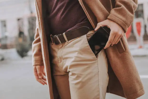 I have to make a phone call. Close up of elegant guy taking modern black cellphone out of trouser pocket