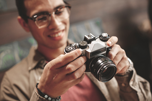 Close up of gentleman in glasses holding old vintage photo camera. Focus on male hands with optical device