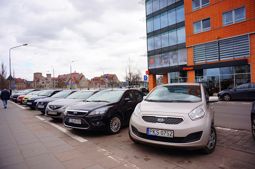 Poznan, Poland - March 8, 2019: Row of parked cars on parking spots close by the Globis office building with Orange telecommunication shop on the Slowackiego street.