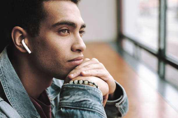 Handsome young man using wireless earphones and resting chin on hands
