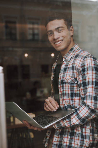 istock Good-looking young man behind glass using laptop 1135936415