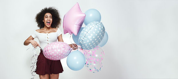 Happy birthday! Positive young afro american woman with curly hair is holding a bunch of colourful balloons and laughing. Web Banner. 16x9 Format. Happiness concept