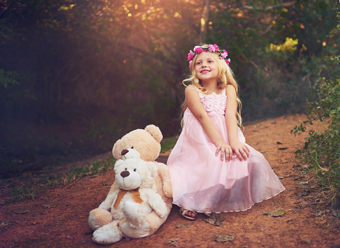 Shot of a happy little girl sitting and waiting with her teddy bears in the middle of a dirt road