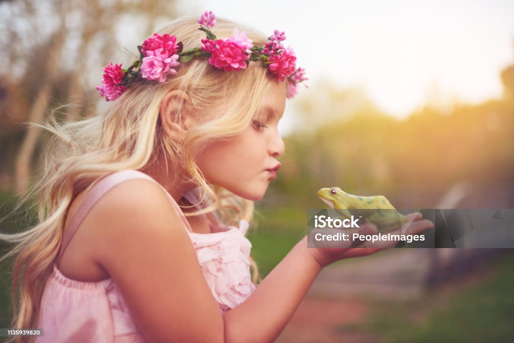 Beauty and the beast Shot of a cheerful little girl holding a frog and going in for a kiss while standing outside in nature Crown - Headwear Stock Photo
