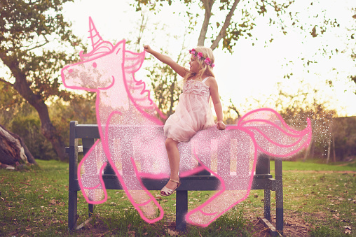 Shot an adorable little girl riding a pink toy unicorn outdoors