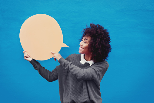 Cropped shot of an attractive young woman holding a speech bubble against a blue background