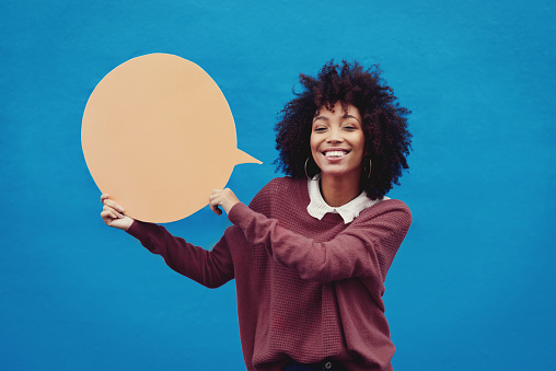 Cropped shot of an attractive young woman holding a speech bubble against a blue background