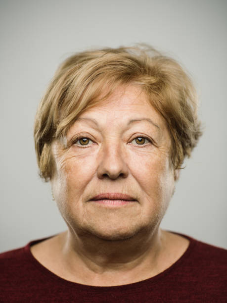 Portrait of real caucasian mature adult woman with blank expression Close up portrait of mature adult caucasian woman with blank expression against gray white background. Vertical shot of spanish real people staring in studio with blond hair. Photography from a DSLR camera. Sharp focus on eyes. pudgy woman pictures stock pictures, royalty-free photos & images