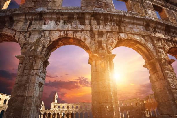 vue sur le clocher d'église par des arches d'amphithéâtre avec le fond de ciel pourpre de lever du soleil - gladiator rome italy sunlight photos et images de collection