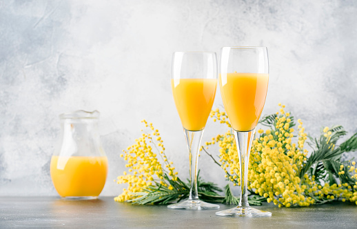Festive alcohol cocktail mimosa with orange juice and cold dry champagne or sparkling wine in glasses, gray bar counter with flowers, place for text, selective focus