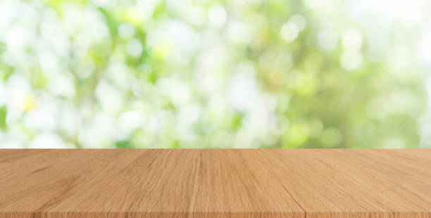 istock abstract blurred greenery leaves of tree park garden with sunlight glow and modern cream color wood plank table for show product on display concept 1135947663