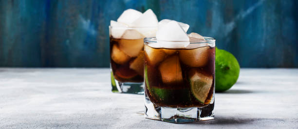 cocktail alcoolique cuba libre avec glace, lime, jus, cola et rhum doré, comptoir de bar gris, focus sélectif - whisky cocktail glass rum photos et images de collection