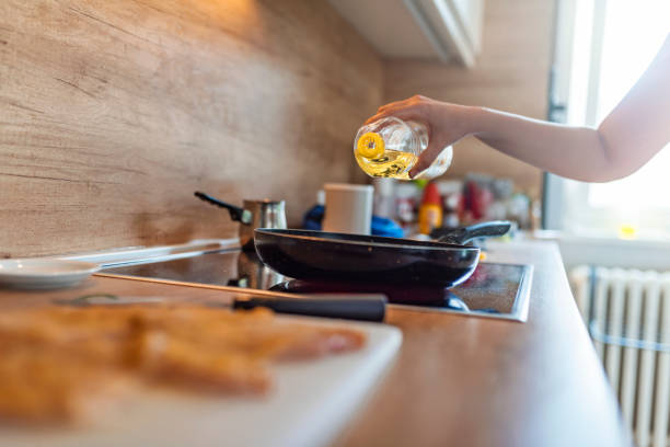 Home cooking.  Photo of Unrecognizable  Caucasian woman pouring oil from a bottle into the pan in the kitchen. Female hand Pouring vegetable oil into frying pan during the day.