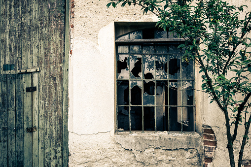 Color image depicting the jagged smashed glass window of an abandoned building. Beyond the broken glass we can see the ruined interior of the building. Room for copy space.