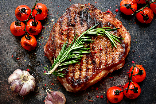 Grilled marbled beef steak with vegetables on a dark slate, stone or concrete background.Top view with copy space.