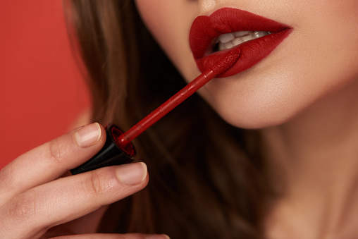 Close up of young lady holding lipstick and applying her lips in studio. Focus on lips. Beauty concept