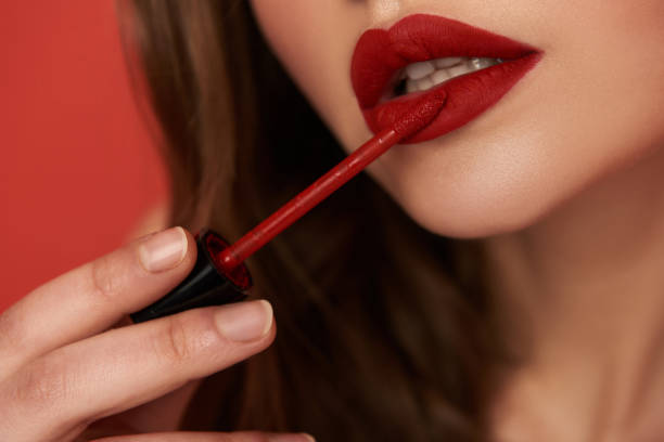 Cropped photo of woman with bright lipstick isolated on red background Close up of young lady holding lipstick and applying her lips in studio. Focus on lips. Beauty concept lipstick stock pictures, royalty-free photos & images