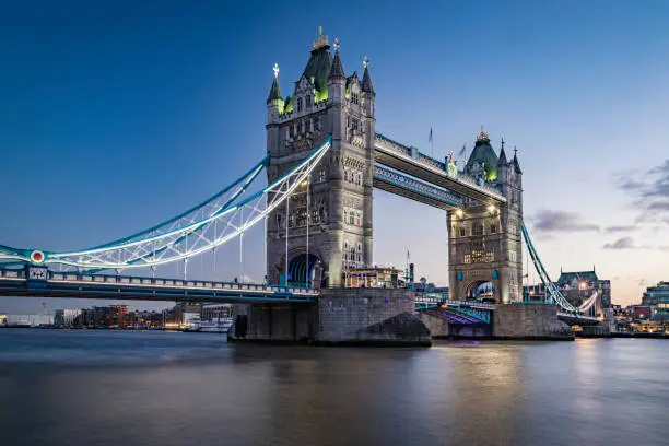 Panoramic high detail view towards Tower Bridge with its colourful evening illumination in downtown London city, England. Long exposure technique to blur the river Thames with plenty of copy space for your message over the water body. Shot on EOS R full frame system with RF premium lens.
