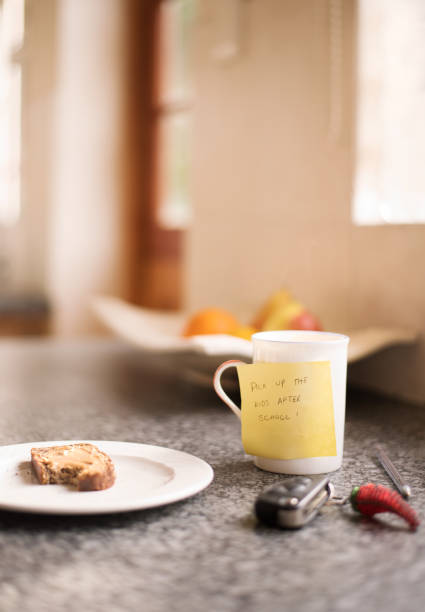 Shot of cup and bread slice on kitchen counter with note for husband to pick up kids after school