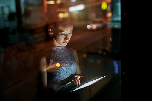 Shot of a young businesswoman using a digital tablet during a late night in a modern office
