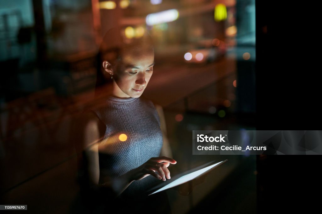 Putting the deadline first Shot of a young businesswoman using a digital tablet during a late night in a modern office Technology Stock Photo