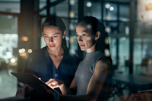 Shot of two young businesswomen using a digital tablet during a late night in a modern office